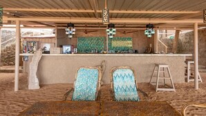 Un espace bar avec un comptoir, deux chaises à motifs, un tabouret et un mur décoratif orné de calligraphies.