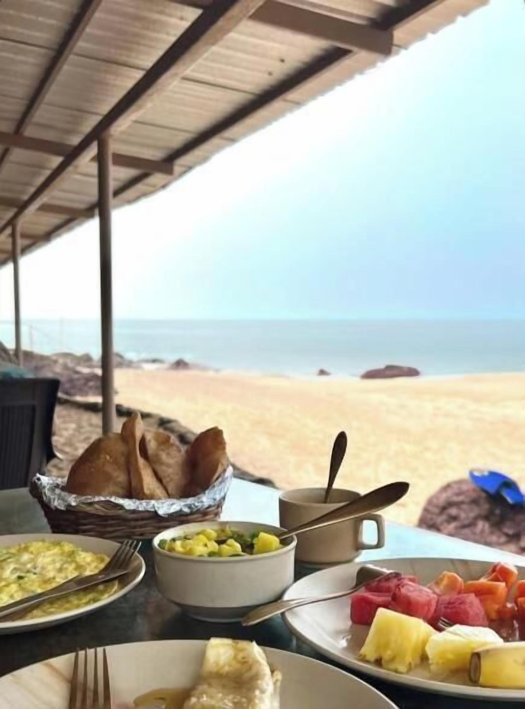 A table with breakfast items, a view of the beach, and a wooden ceiling.