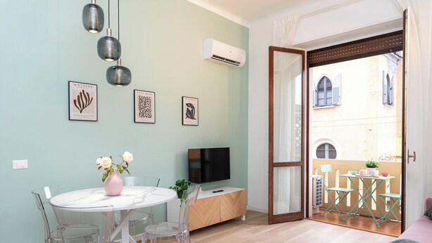 A modern living room with a round dining table, clear chairs, a pink vase with flowers, a flat-screen TV, and artwork on the wall. - VivimiHome - La Stella dei Navigli (Milan)