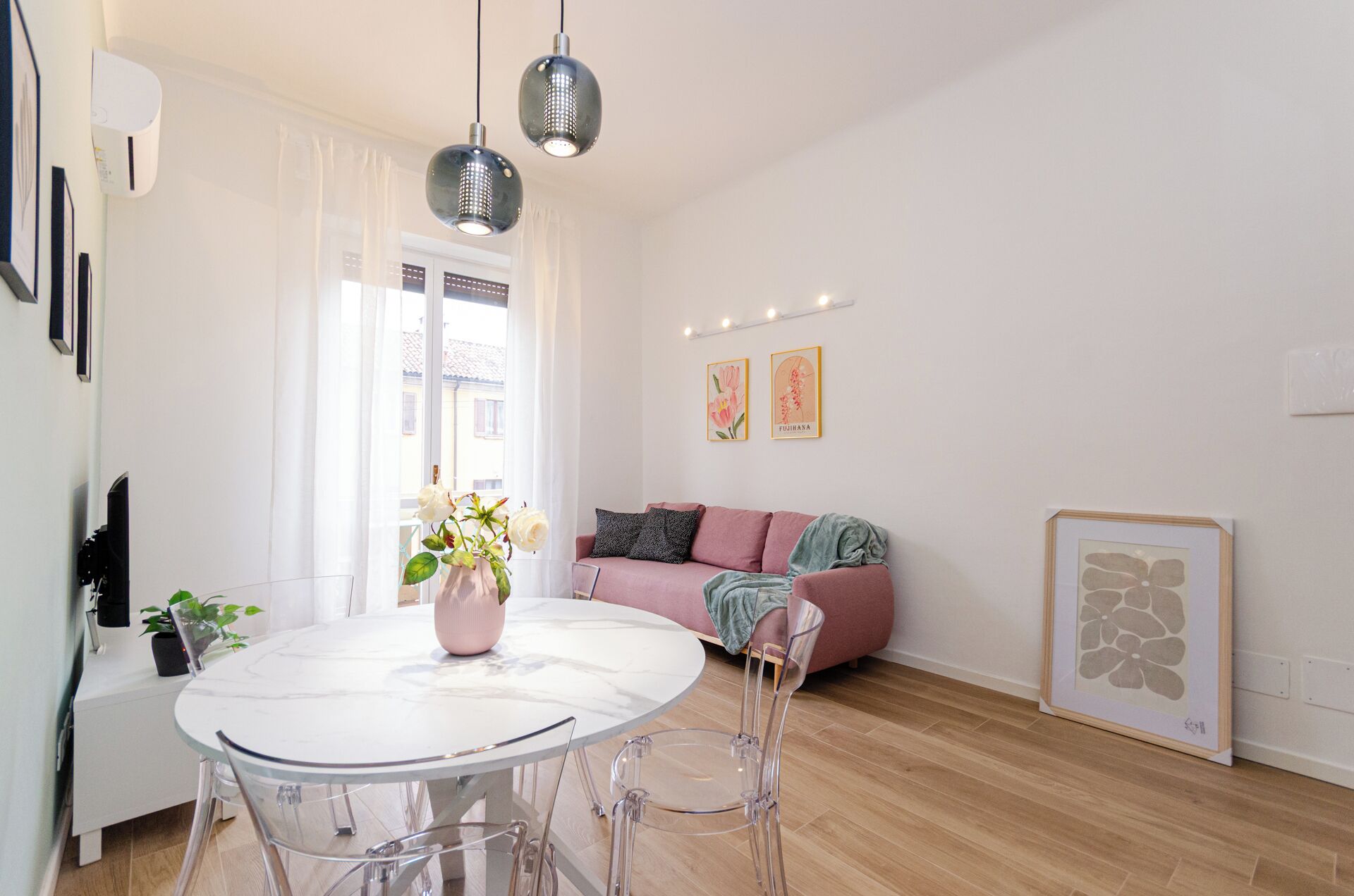 A modern living room with a round dining table, clear chairs, a sofa, and a window with curtains.