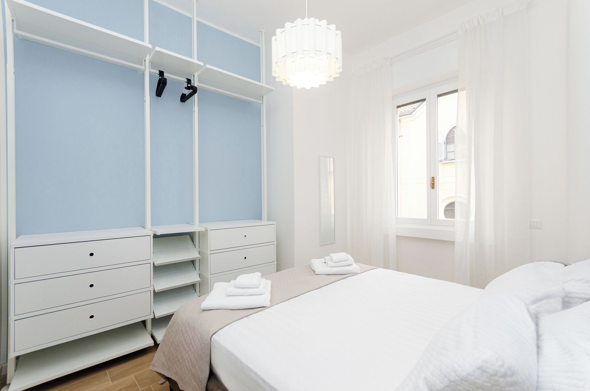 A bedroom with a bed, a wardrobe, a mirror, and a window with curtains.