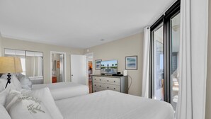 Habitación de hotel con dos camas, un aparador, un televisor y vista al mar.