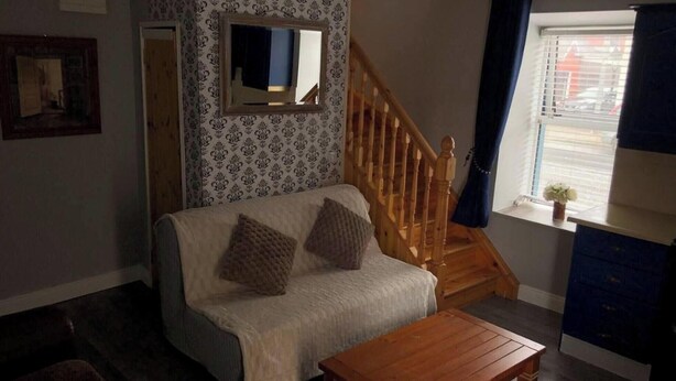 Een woonkamer met een bank, een houten salontafel, een spiegel, een trap en een raam met jaloezieën.