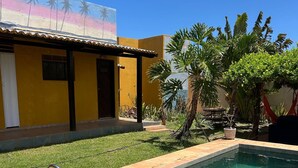 A swimming pool with a Brazilian flag float, a yellow building with a mural, and tropical plants. - Beautiful and cozy room in Casa 7 Mares (Rio Grande do Norte city)