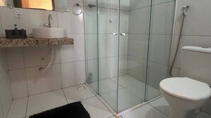 A bathroom with a glass shower enclosure, a toilet, a sink with a marble countertop, and a black rug on the floor.