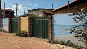A gated property with a sandy driveway, a brick wall, and a mural of a beach scene. - Nice and cozy room with pool (São Miguel do Gostoso)