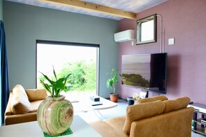 Un salon moderne avec un canapé, une table basse, un téléviseur et une grande fenêtre donnant sur un paysage verdoyant.