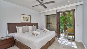 Un dormitorio con cama, ventilador de techo, mesita de noche, ventana y vistas al exterior.
