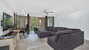 Una sala de estar moderna con un sofá modular, un televisor de pantalla plana, un escritorio con una computadora y un ventilador de techo.