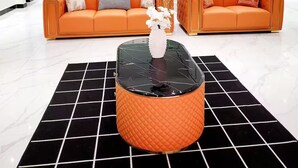 Una sala de estar moderna con dos sofás naranja, una mesa de centro de vidrio y una escalera con barandillas de cristal.