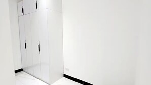 Un pasillo con paredes blancas y suelo de baldosas que conduce a una habitación con un armario blanco.