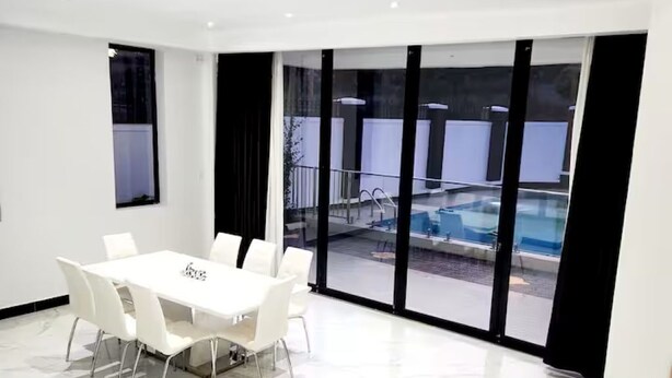 Una sala de conferencias moderna con una mesa y sillas blancas, ventanas amplias y vistas a una piscina al aire libre.