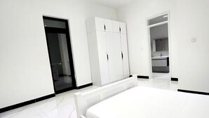 Un dormitorio con una cama grande, un armario blanco y un baño visible a través de una puerta abierta.