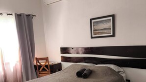 A neatly made bed with a patterned bedspread, a wooden nightstand with a lamp, a framed picture on the wall, and a window with curtains. - Marina Loft unit 2 floor, #201 (Del Coco Beach)