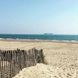 A sandy beach with a wooden fence in the foreground and a building in the distance. - Magnificent Camping Les Sables in Cap d'Agde (Agde)