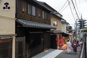 Ein traditionelles japanisches Gebäude mit Holzfassade, einem schwarzen Tor und einem kleinen Außenbereich mit roten Pflanzen.