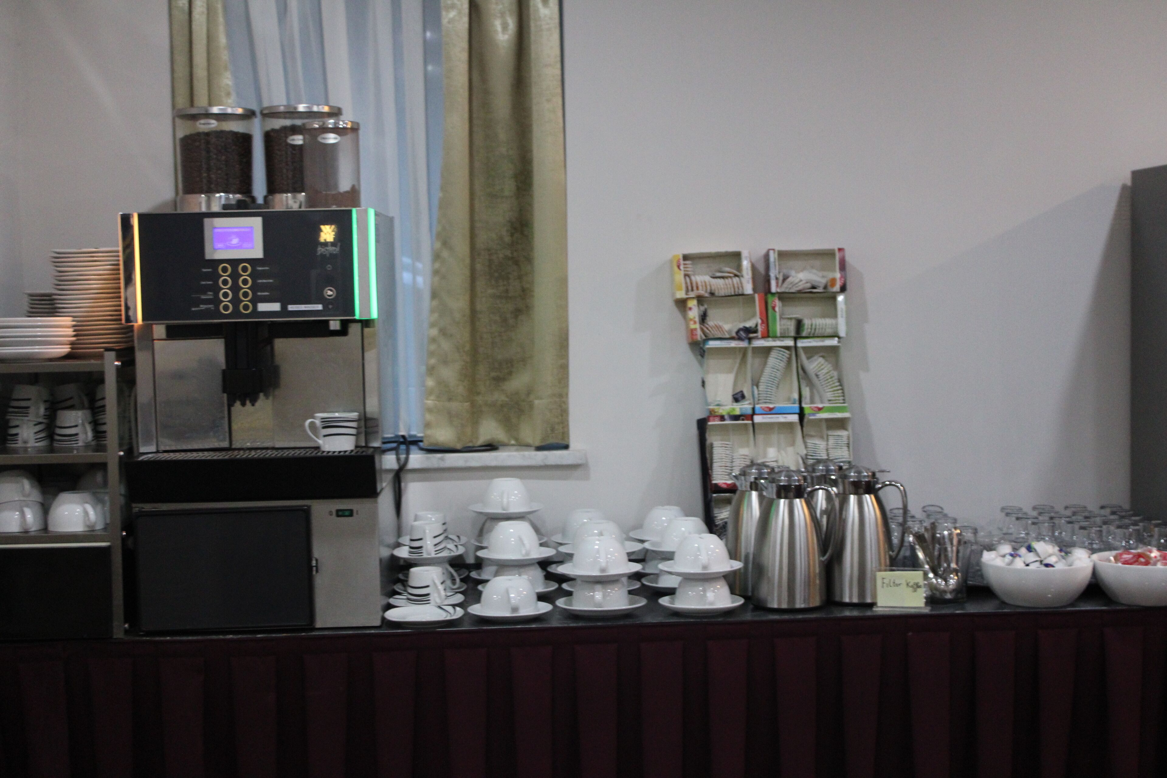 Una estación de café con una máquina de café, tazas y un refrigerador pequeño.