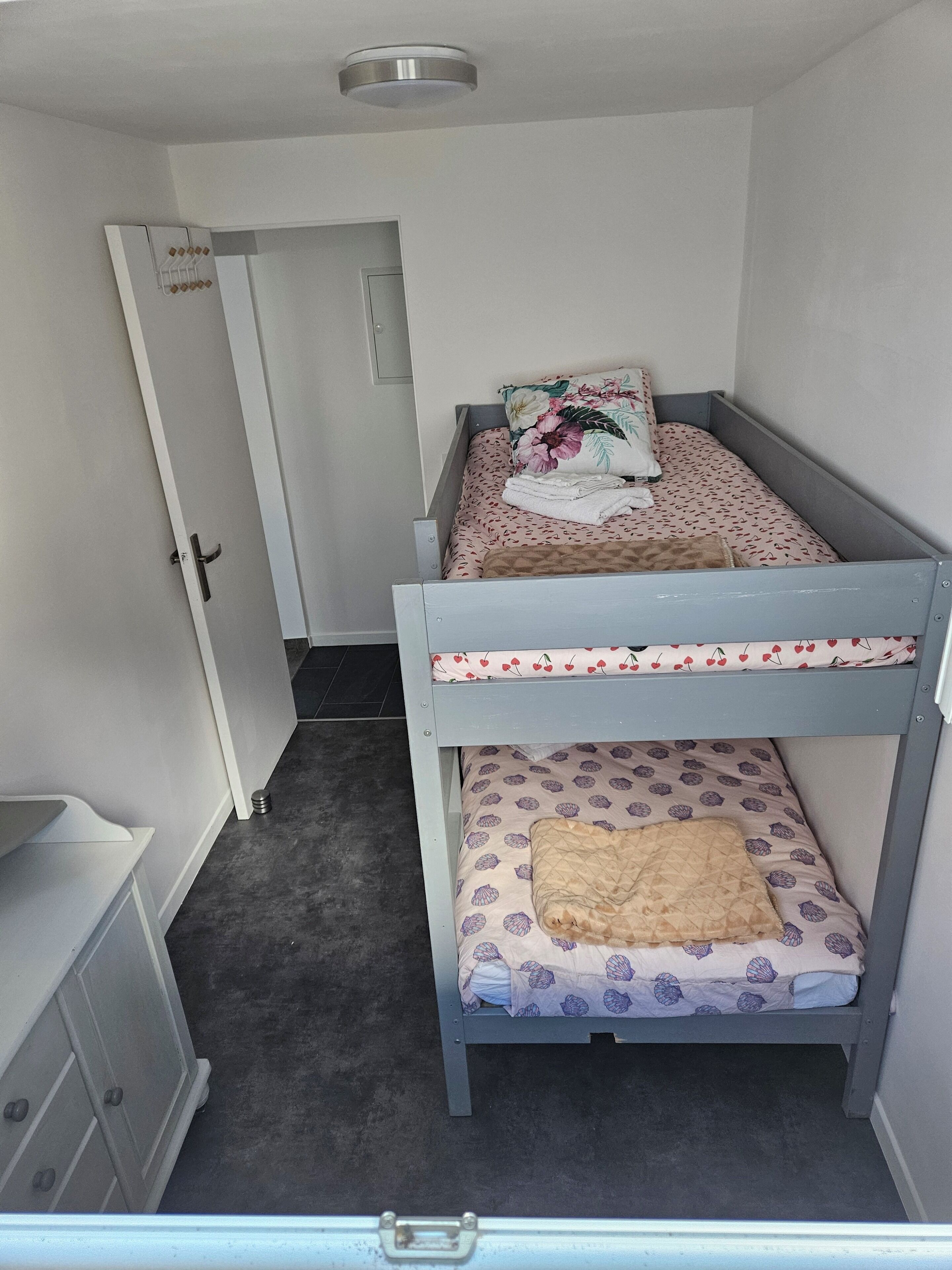 A bunk bed room with a door, a small cabinet, and a grey floor.
