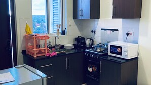 Une cuisine de taille réduite, équipée d’une cuisinière, d’un four à micro-ondes, de placards et d’une fenêtre avec des stores.
