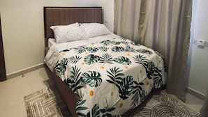 Une chambre à coucher avec un lit, un ventilateur de plafond, un climatiseur, des rideaux et un tapis à motifs.