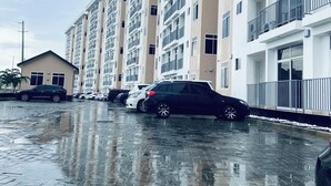 Un immeuble résidentiel à plusieurs étages, doté de balcons, d’un espace de stationnement et d’un petit bâtiment avec un toit en pente.