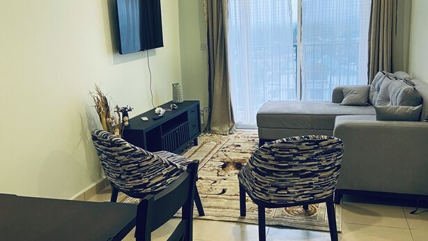 Un salon avec un canapé, deux fauteuils à motifs, un téléviseur et une fenêtre avec des rideaux.