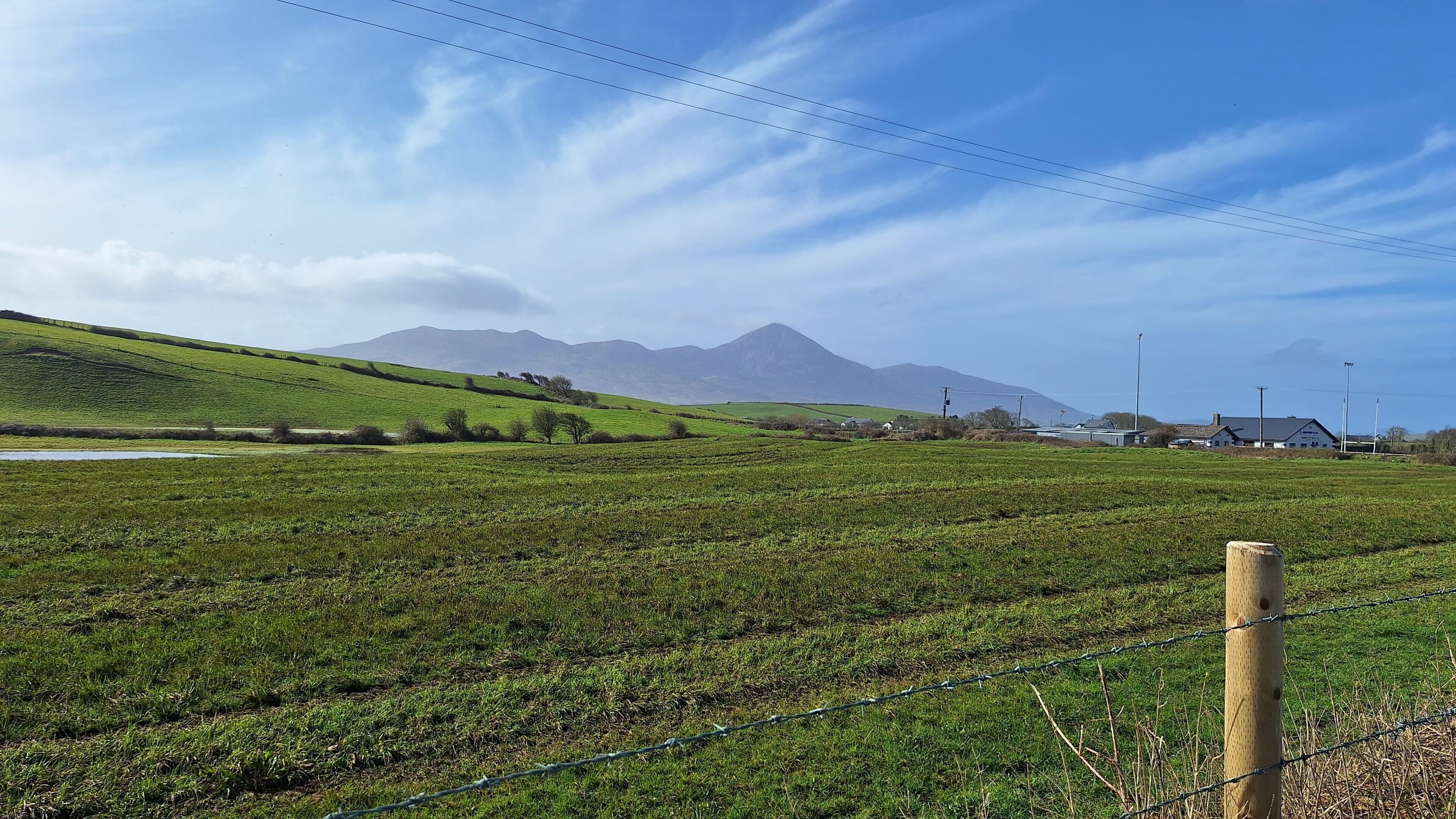 Eine ländliche Landschaft mit einem Feld, einem Zaun und fernen Bergen.