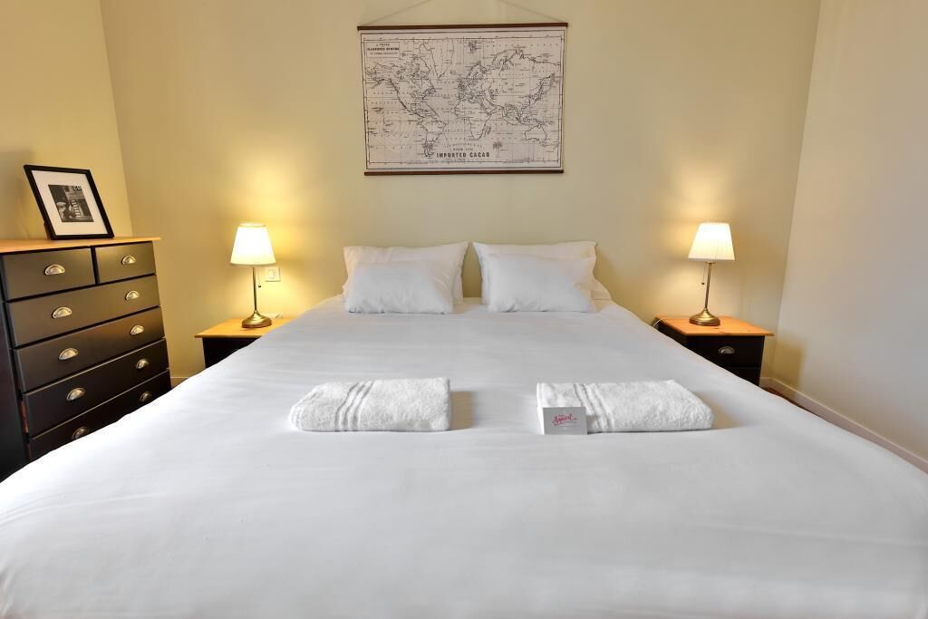 A neatly made bed with white linens, two bedside lamps, a dresser with drawers, and a world map on the wall.
