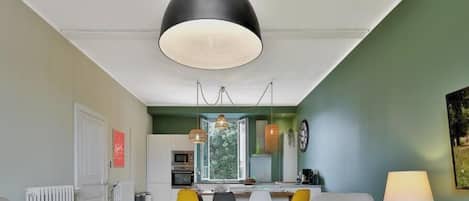 Una cocina moderna con un ventanal grande, luces colgantes y un comedor con sillas amarillas.