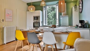 A modern kitchen with a dining area, large windows, and a view of greenery.