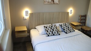 A neatly made bed with two pillows, a headboard, bedside tables, and a wall-mounted light fixture. - Comfortable 44 M2 house, 3* Gîte de France, 100 m from stock pond. (Kerprich-aux-Bois)