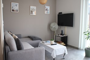 A living room with a grey sofa, a white table, a TV, and framed pictures on the wall.