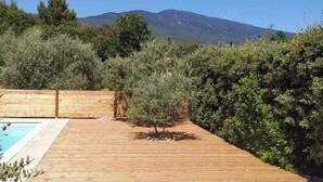 A wooden deck with a pool, surrounded by dense greenery and mountains in the background. - Magnificent villa at the foot of Mont Ventoux (Bédoin)