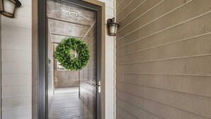 Une porte ornée d’une guirlande, une terrasse en bois et un luminaire fixé au mur.