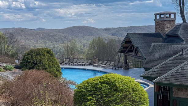 Une piscine entourée de chaises longues, un bâtiment en pierre doté d’une cheminée, et un paysage montagneux en arrière-plan.