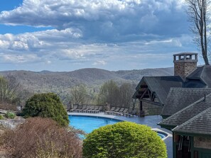 A pool with lounge chairs, a stone building with a chimney, and a mountainous backdrop. - 1BR Condo w/ Stunning Long-Range Views, Deck + Hot Tub / Pool / Gym - Near Boone (Boone)