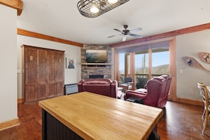 A spacious room with a wooden table, leather chairs, a stone fireplace, a ceiling fan, and a large window with a view. - 1BR Condo w/ Stunning Long-Range Views, Deck + Hot Tub / Pool / Gym - Near Boone (Boone)