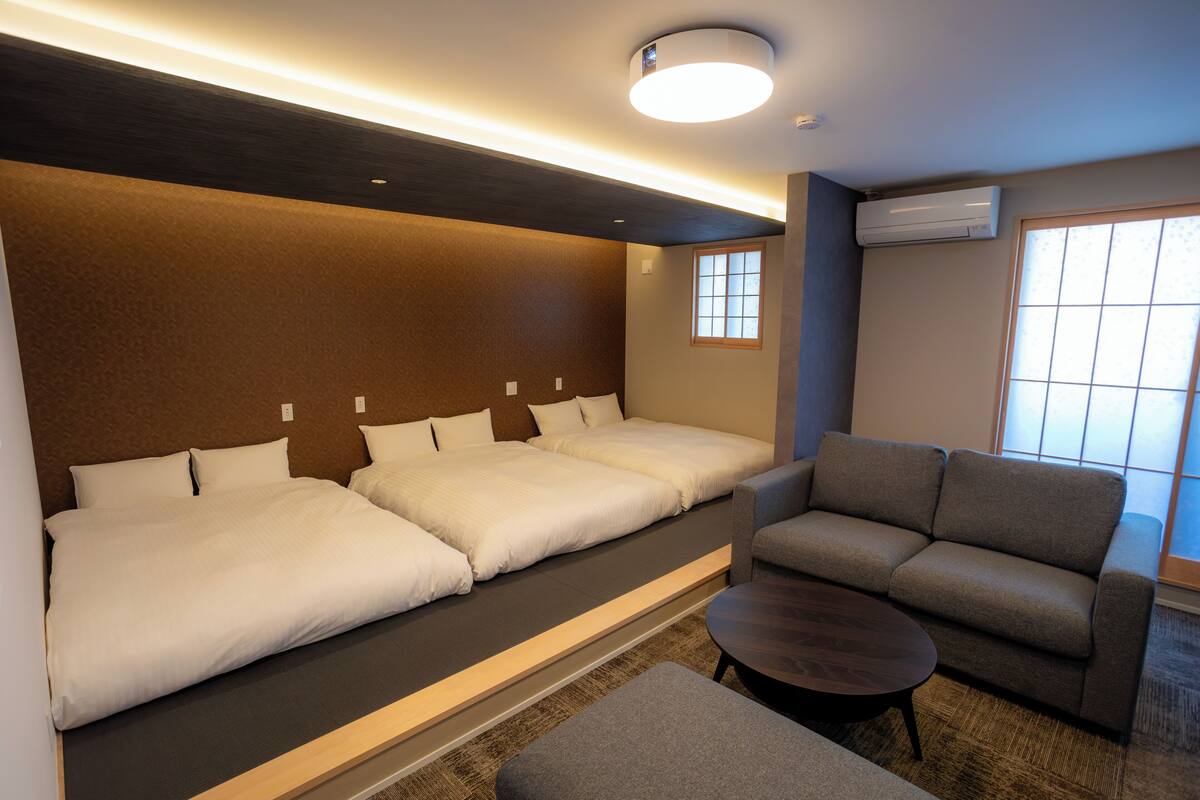 Ein Hotelzimmer mit zwei Betten, einem Schlafsofa, einem kleinen Tisch und einer Klimaanlage.