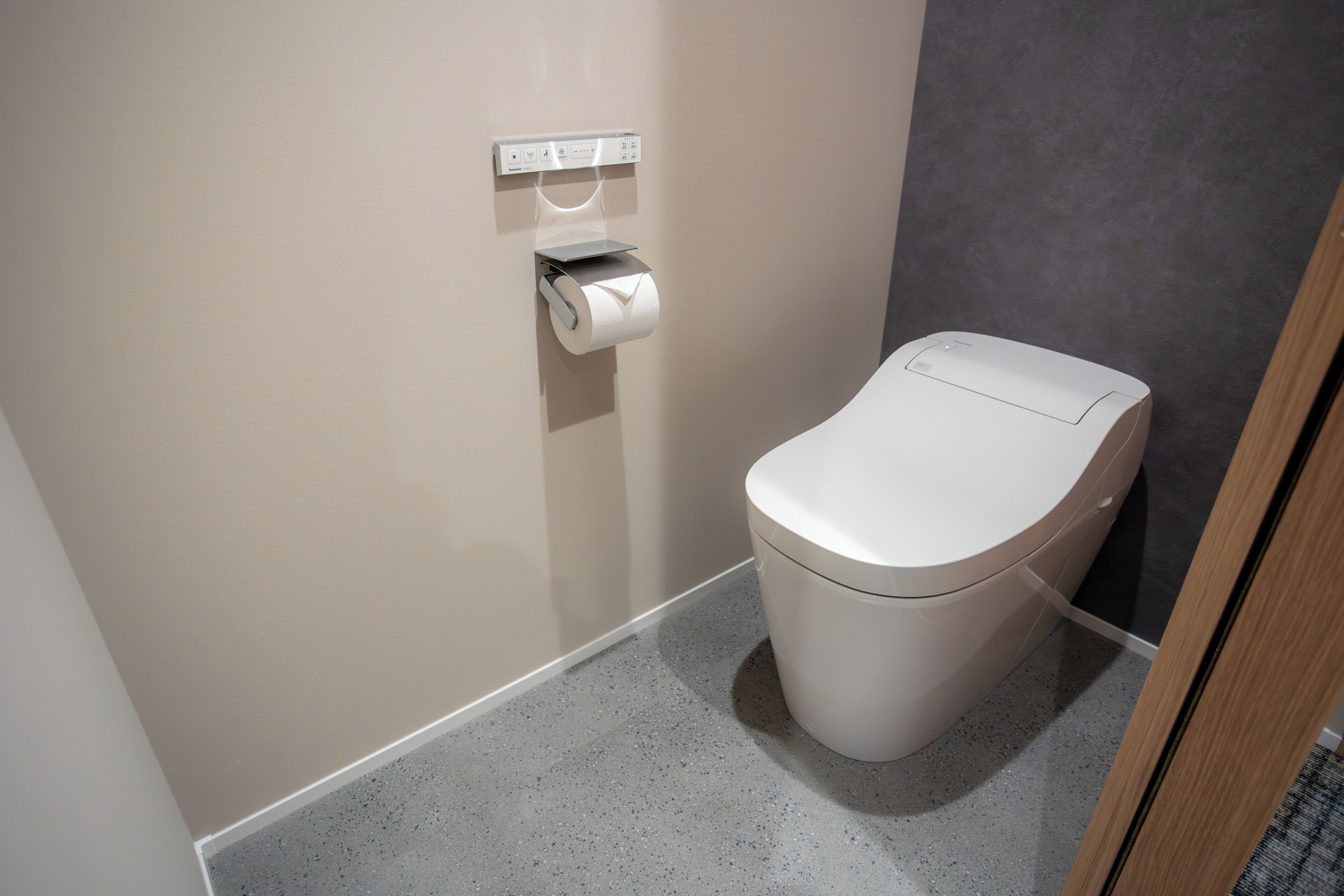 A modern bathroom with a toilet, a paper towel dispenser, and a wall-mounted electrical outlet.