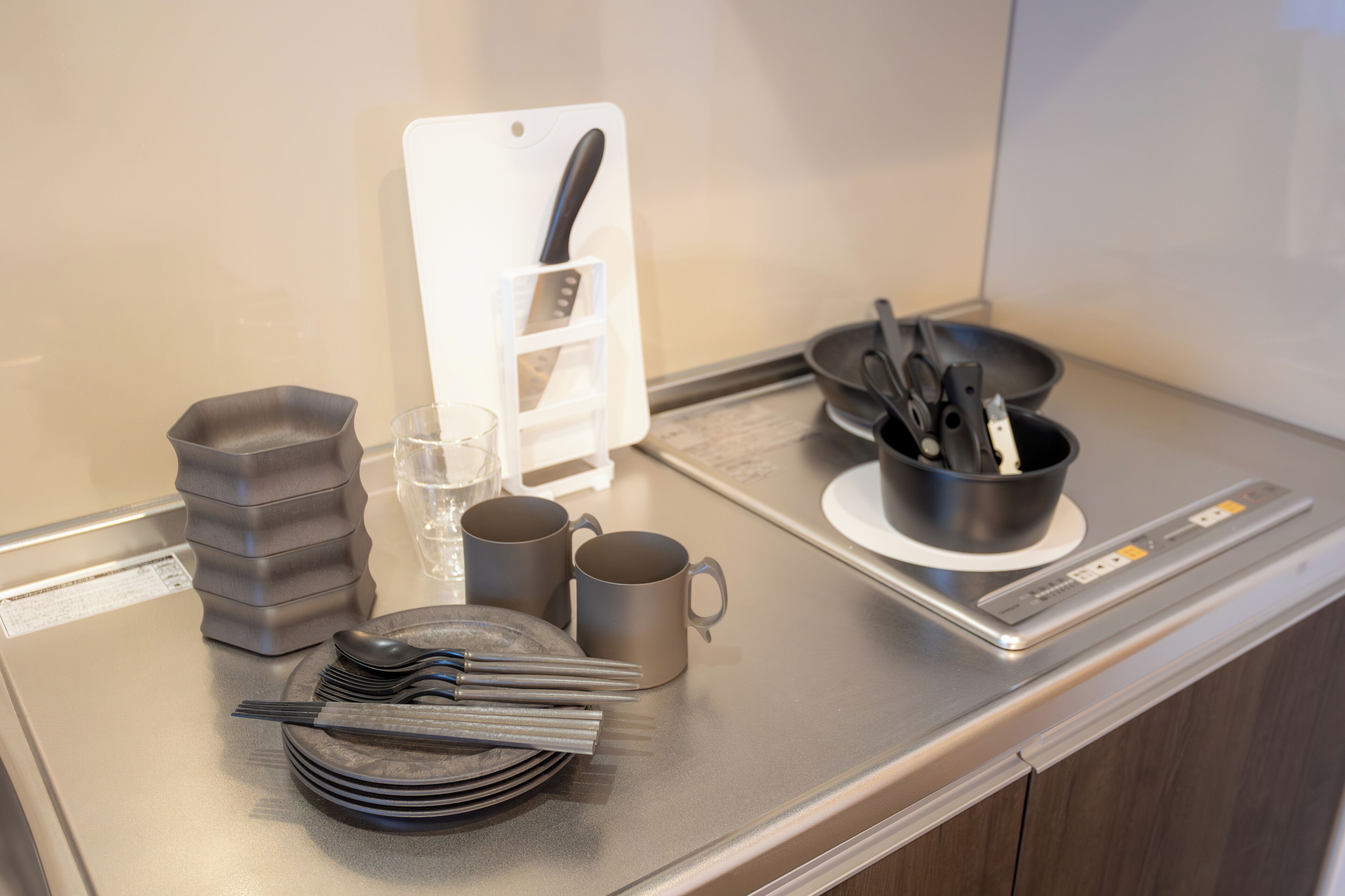 Un plan de travail de cuisine avec une planche à découper, un porte-couteaux, une poêle, des assiettes, des tasses et des ustensiles.