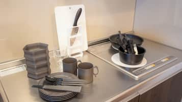 Un plan de travail de cuisine avec une planche à découper, un porte-couteaux, une poêle, des assiettes, des tasses et des ustensiles.