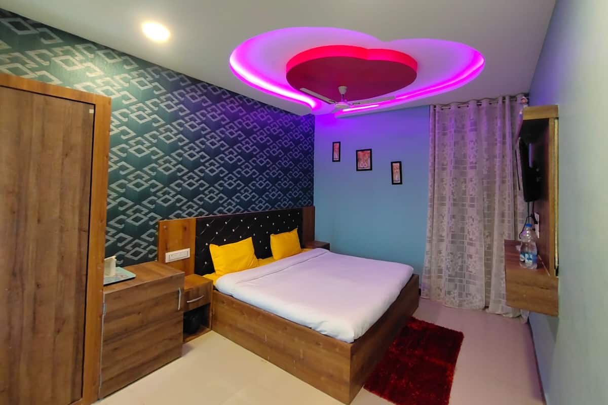 Une chambre à coucher avec un lit en bois, une table de chevet, une armoire, un luminaire au plafond et un téléviseur fixé au mur.