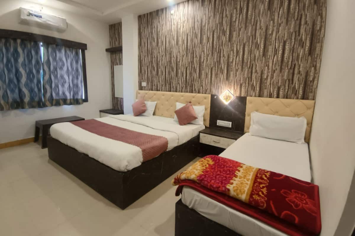 Une chambre d’hôtel avec un grand lit, un lit plus petit, une table de chevet, un miroir et un mur décoré d’un motif.