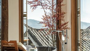 A room with a large window, a bathtub, and a wooden bench with a book and a small cake. - Zome Yunju· Skyview Villa, Lijiang Old Town (Lijiang)