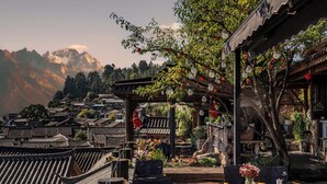 A traditional wooden building with a sloped roof, outdoor seating area with chairs and tables, and a view of mountains in the background. - Zome Yunju· Skyview Villa, Lijiang Old Town (Lijiang)