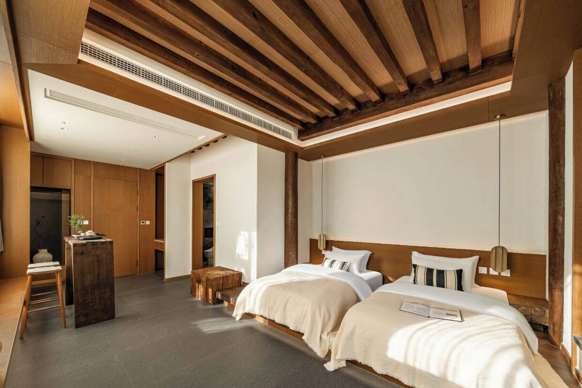 A modern hotel room with two beds, a wooden ceiling, and a minimalist design.