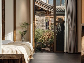 A bedroom with a bed, a potted plant, a small table, and a view of an outdoor area with a stone wall and a traditional roof. - Zome Yunju· Skyview Villa, Lijiang Old Town (Lijiang)