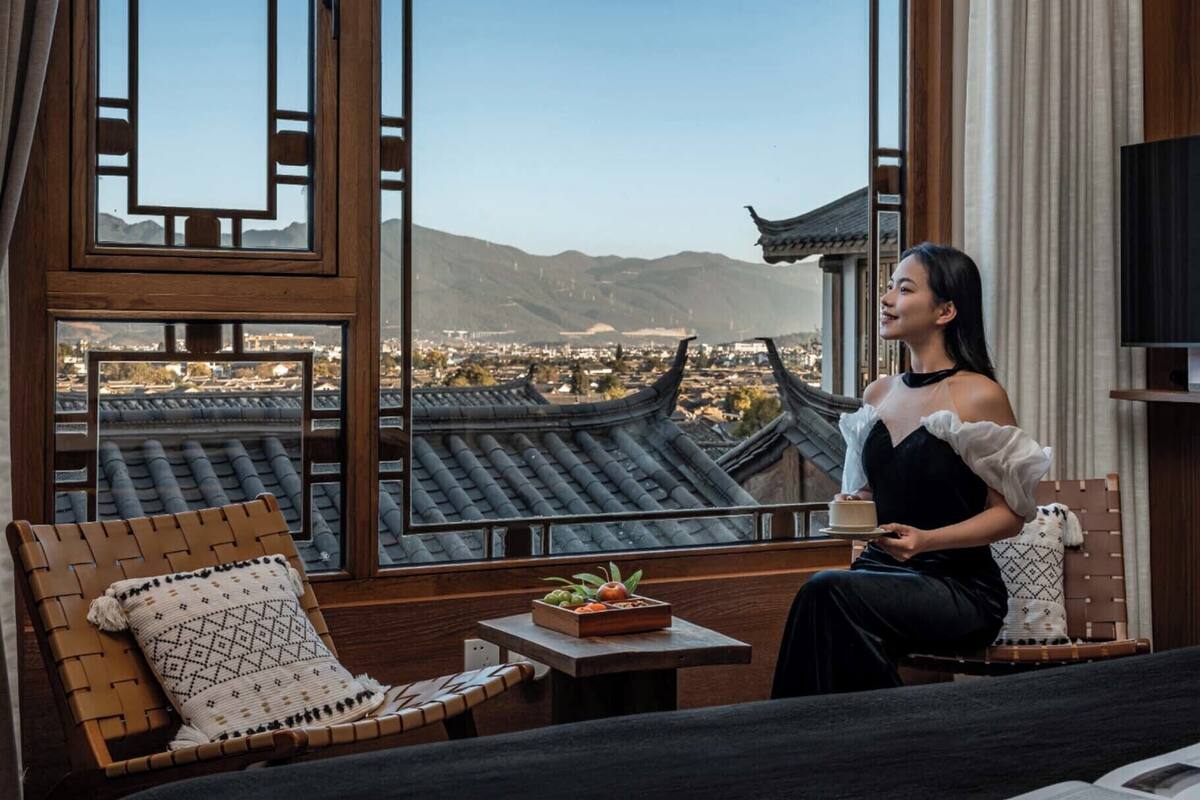 A room with a view of traditional architecture, a dining table with a fruit bowl, and a person seated.