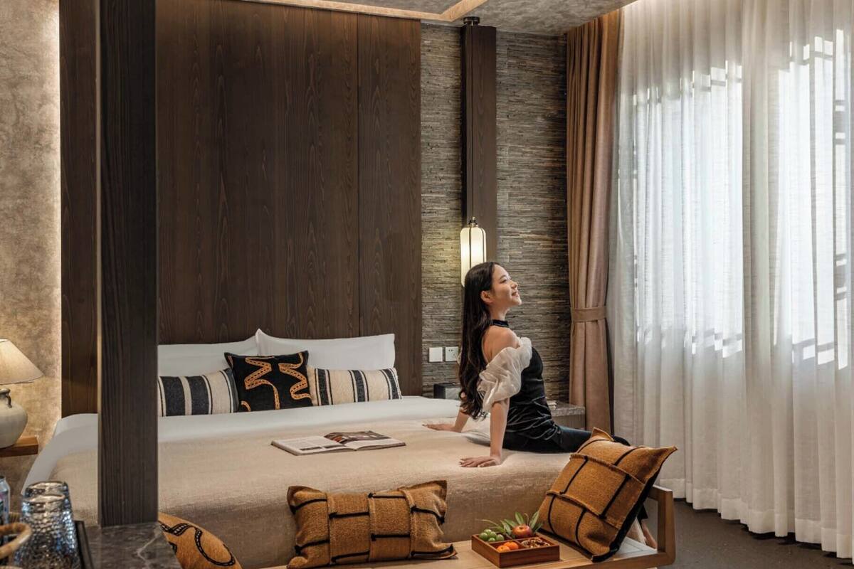 A modern hotel room with a large bed, a sitting area with a table, and a view of the outdoors through sheer curtains.