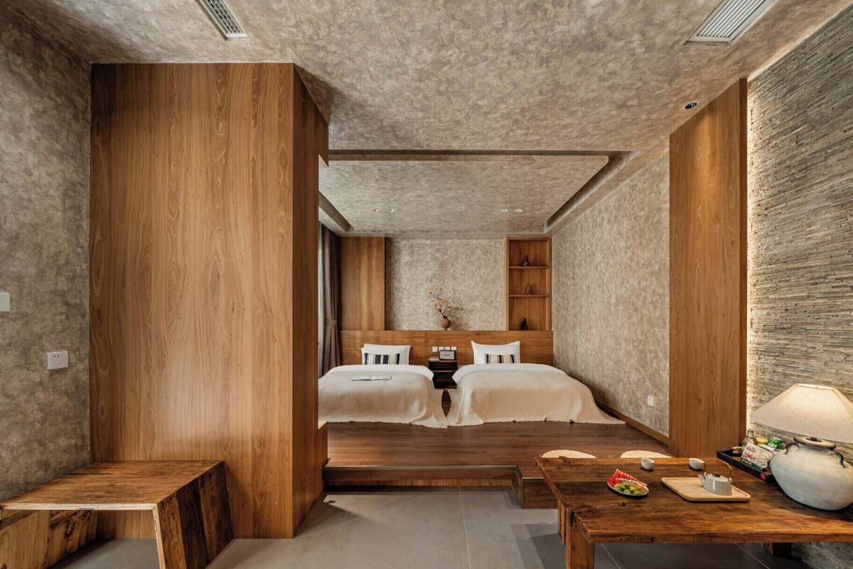 A modern bedroom with a large bed, wooden furniture, and a stone accent wall.